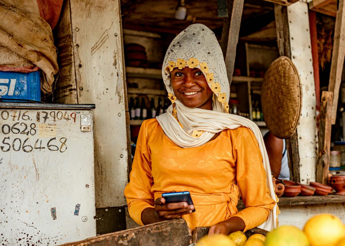 Market trader using a mobile phone, reflecting digital services and consumer growth in African markets